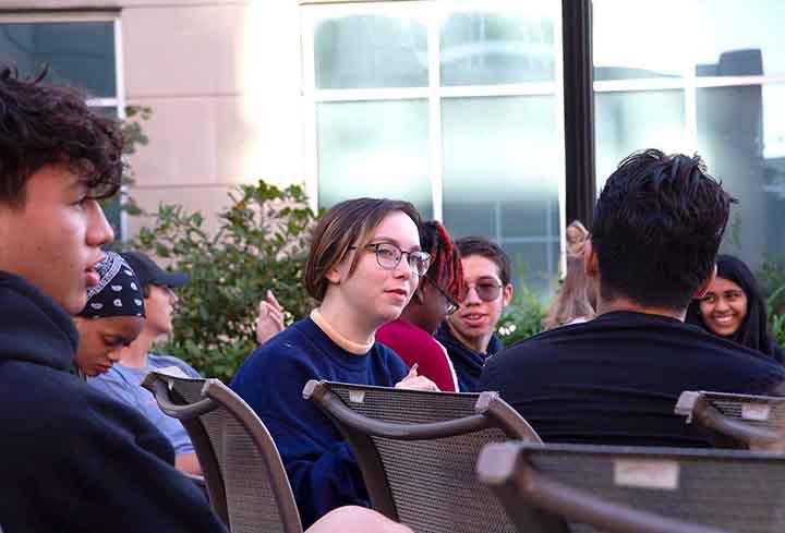 A group of students sit in chairs on an outside patio