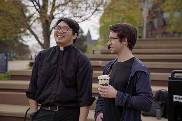 A young Jesuit laughs while chatting with another young man in the plaza of the clock tower.